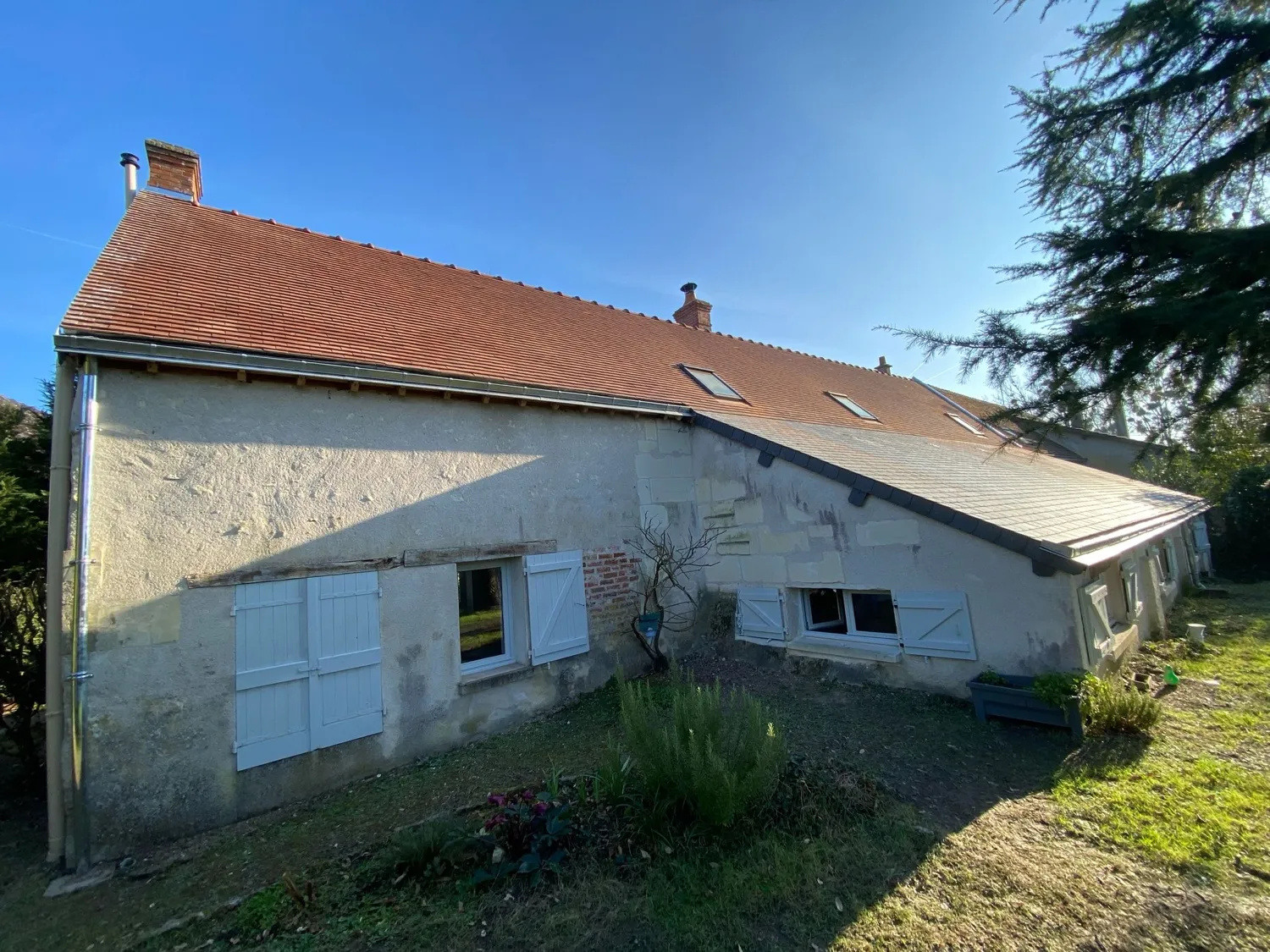 Maison ancienne aux volets blancs sous ciel bleu