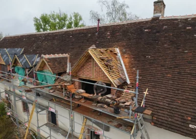 Couvreur rénovant une toiture en tuiles sur échafaudage