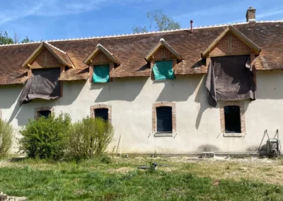 Maison ancienne aux lucarnes bâchées sous ciel bleu