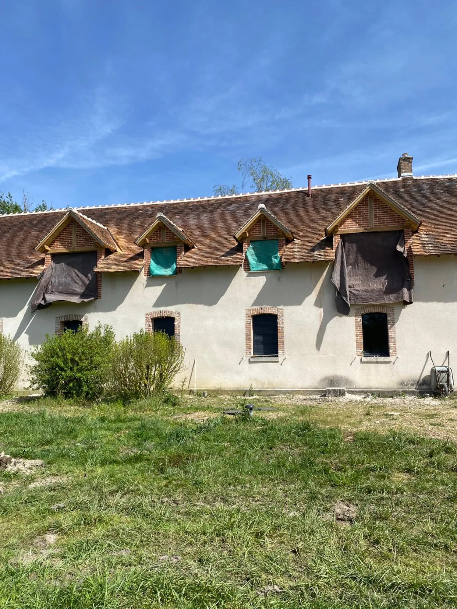 Maison ancienne aux lucarnes bâchées sous ciel bleu