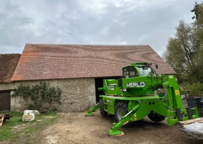 Nacelle télescopique verte devant une grange en pierre