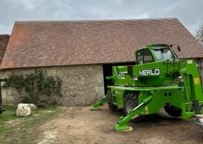 Chariot télescopique vert devant grange en pierre
